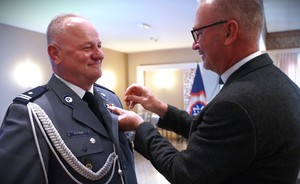 Ksiądz wręcza medal policjnantowi.